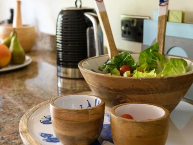 A wooden salad bowl with lettuce and cherry tomatoes with two wooden cups on a kitchen counter at Ty Bach - Beaumaris in Beaumaris