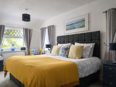 A bedroom with a large bed with yellow and blue pillows and a yellow throw at Ty Bach - Beaumaris in Beaumaris