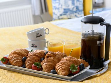 A tray with croissants strawberries blueberries two glasses of orange juice a French press coffee maker and stacked coffee cups on a yellow surface at Ty Bach - Beaumaris in Beaumaris