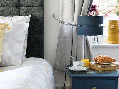 A bedroom with a bed and pillows next to a nightstand with a lamp cup of coffee glass of orange juice croissants and books at Ty Bach - Beaumaris Beaumaris