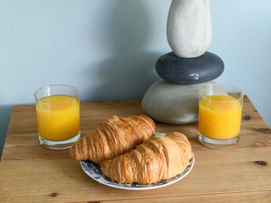 Two croissants on a plate with two glasses of orange juice and stacked stones on a wooden table at Ty Bach - Beaumaris in Beaumaris