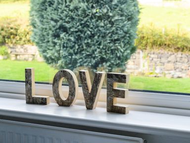 Wooden letters spelling love on a white windowsill with a garden outside at Ty Bach - Beaumaris in Beaumaris