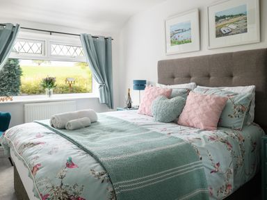A bedroom with a bed with pillows and folded towels near a window with curtains at Ty Bach - Beaumaris in Beaumaris