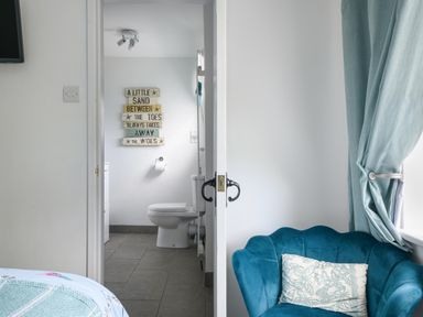 A bathroom with a toilet and a sign on the wall next to a room with a blue armchair and blue curtains at Ty Bach - Beaumaris in Beaumaris