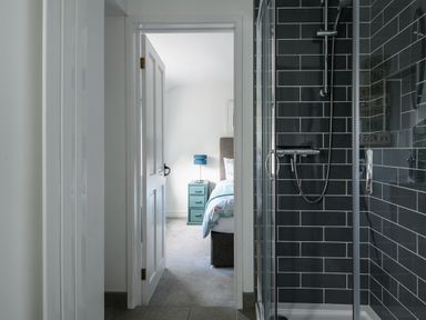 A shower with black tiles and a door open to a bedroom with a bedside table and lamp at Ty Bach - Beaumaris in Beaumaris
