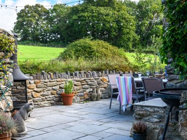 An outdoor patio with a stone wall dining table and chairs with colorful towel and string lights at Ty Bach - Beaumaris