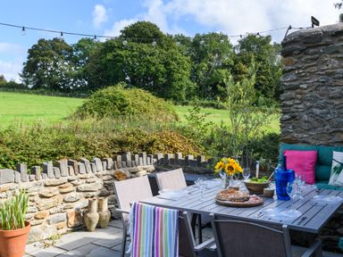 An outdoor dining area with a table set with plates glasses and food next to a stone wall and green field at Ty Bach Beaumaris