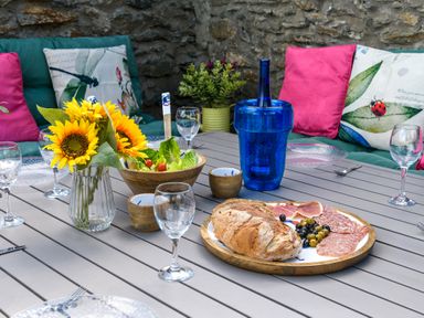 An outdoor dining table with bread olives charcuterie a salad bowl a blue bottle sunflowers and glassware at Ty Bach - Beaumaris in Beaumaris