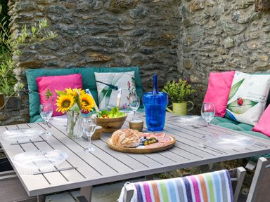 An outdoor dining table set with bread salad and glasses surrounded by cushioned seating with pillows at Ty Bach - Beaumaris in Beaumaris