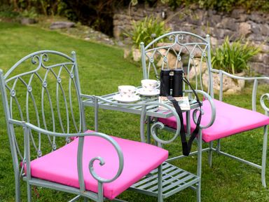A garden setting with metal chairs with pink cushions two teacups on a small table binoculars and a book on the table at Ty Bach - Beaumaris in Beaumaris