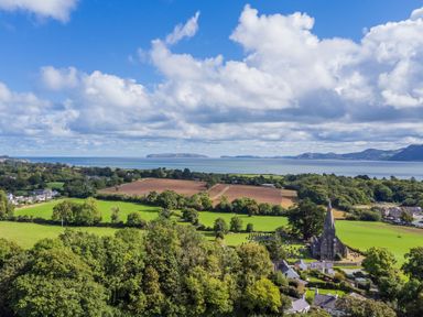 A coastal landscape with fields trees a church and sea in the background at Ty Bach Beaumaris