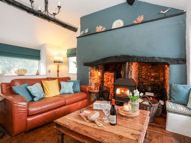 A living room with a leather sofa cushions a wooden coffee table a wood-burning stove and a window seat at Ty Bach - Beaumaris in Beaumaris