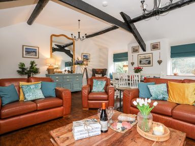 A living room with leather sofas cushions a wooden coffee table and dining area at Ty Bach Beaumaris