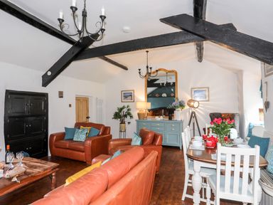 A living room with leather sofas a wooden dining table with white chairs and a sideboard with a mirror at Ty Bach - Beaumaris in Beaumaris