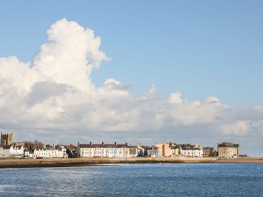 A coastal town with pastel colored buildings along a waterfront under a blue sky at Ty Bach - Beaumaris in Beaumaris