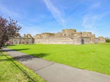 A stone castle surrounded by green grass and a playground next to a pathway at Ty Bach - Beaumaris in Beaumaris