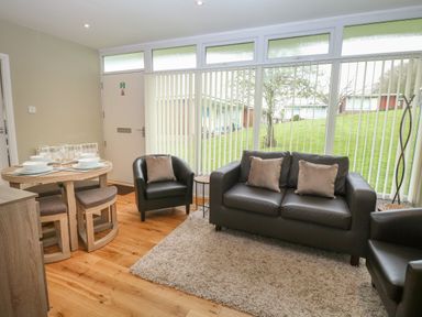 A living room with leather sofa and chairs beside a dining table with tableware at 107 Kings Chalet Park in Cromer