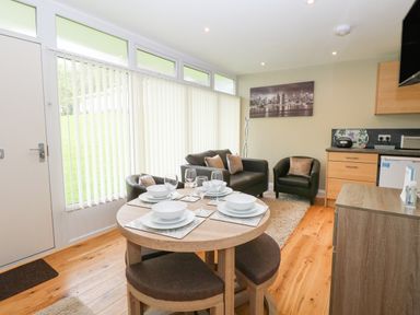 A small dining table set for four next to a seating area with two armchairs and a sofa at 107 Kings Chalet Park in Cromer