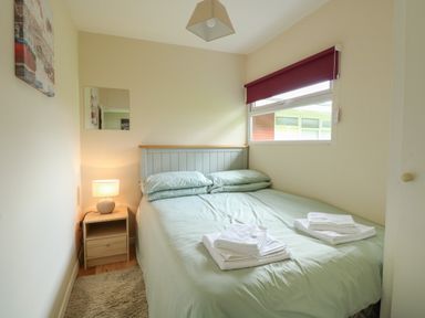 A bedroom with a bed with pillows and folded towels and a bedside table with a lamp at 107 Kings Chalet Park in Cromer