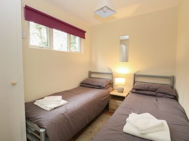 A bedroom with two single beds a nightstand with a lamp a small rectangular mirror and folded towels at 107 Kings Chalet Park in Cromer