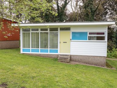 A single story building with large windows a yellow door and blue panels on a grassy lawn at 107 Kings Chalet Park in Cromer