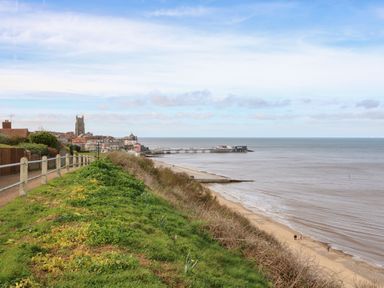 A coastal town with a church tower a pier a sandy beach and a grassy cliffside in Cromer