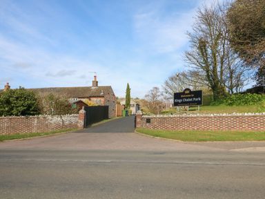 The entrance to Kings Chalet Park with a brick wall and sign near a road in Cromer