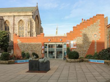 The entrance of Cromer Museum with brick and flint walls and glass doors surrounded by plants and a paved area at 107 Kings Chalet Park in Cromer
