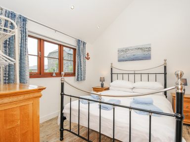 A bedroom with a black metal bed frame bedside tables with lamps a wooden dresser and a window with blue curtains at Pol Glas Cabin in Churchtown near Mullion