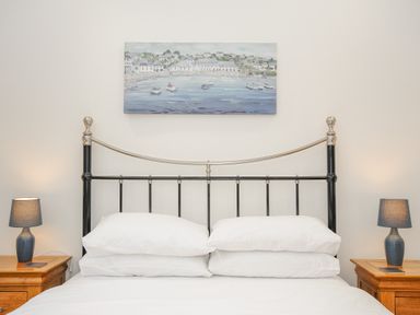 A bedroom with a metal bed frame two bedside tables with lamps and a painting above the bed at Pol Glas Cabin in Churchtown near Mullion