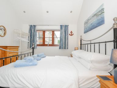 A bedroom with a double bed white bedding blue towels wooden furniture and a window with blue curtains at Pol Glas Cabin Churchtown near Mullion