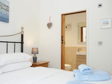 A bedroom with a bed pillow bedside table lamp and an open door leading to a bathroom at Pol Glas Cabin in Churchtown near Mullion