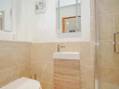 A bathroom with a toilet a small sink wooden cabinet beige tiled walls and a mirror at Pol Glas Cabin Churchtown near Mullion
