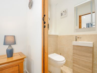 A small bathroom with a toilet a sink and a mirror next to a wooden cabinet with a blue lamp at Pol Glas Cabin Churchtown near Mullion