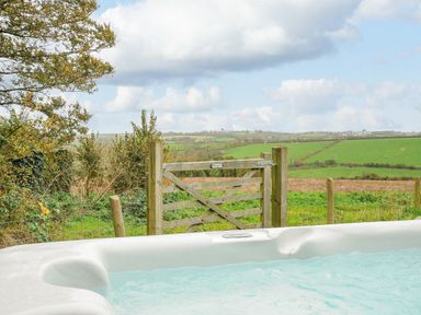 A hot tub in front of a wooden gate with fields and cloudy sky in the background at Pol Glas Cabin in Churchtown near Mullion