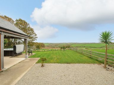 A garden with a covered patio hot tub and chairs overlooking fields at Pol Glas Cabin in Churchtown near Mullion