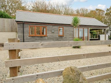 A wooden cabin with gravel yard and wooden fence at Pol Glas Cabin in Churchtown near Mullion