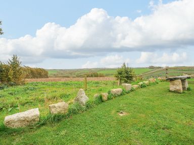 A grassy outdoor area with large stones arranged in a line and trees in the background at Pol Glas Cabin in Churchtown near Mullion
