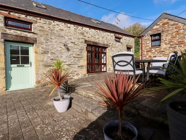 An outdoor patio area with potted plants stone walls two stone buildings a table with four chairs and a green door at Great Meadow Barn in Crantock