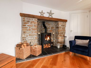 A stone fireplace with a wood-burning stove and baskets of firewood in a living room at Great Meadow Barn in Crantock