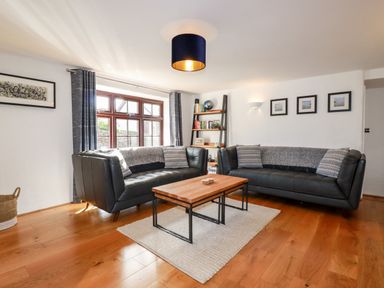 A living room with two black leather sofas a wooden coffee table a bookshelf and framed pictures at Great Meadow Barn in Crantock