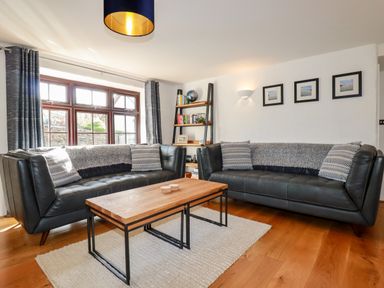 A living room with two black sofas a wooden coffee table a bookshelf and three pictures on the wall at Great Meadow Barn in Crantock
