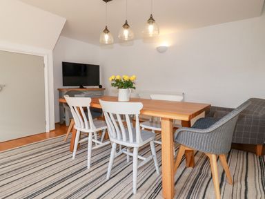 A dining room with a wooden table white and gray chairs a striped rug and a TV at Great Meadow Barn in Crantock