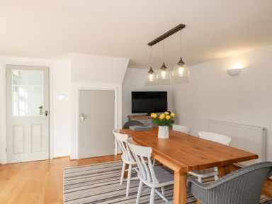 A dining room with a wooden table and chairs a TV on a cabinet and pendant lights at Great Meadow Barn in Crantock