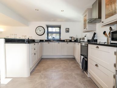 A kitchen with white cabinets black countertops a oven and a window above the sink at Great Meadow Barn in Crantock