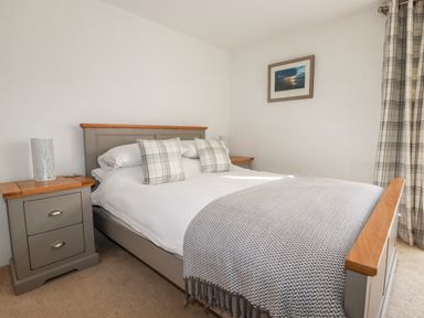 A bedroom with a bed flanked by two nightstands and plaid curtains at Great Meadow Barn in Crantock
