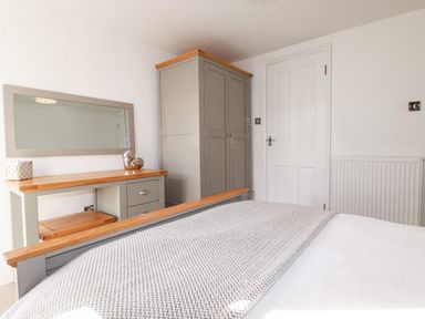 A bedroom with a bed, a wardrobe, a dressing table with a mirror and decorative items at Great Meadow Barn Crantock