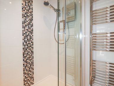 A bathroom shower area with a handheld showerhead and mosaic tile strip at Great Meadow Barn in Crantock