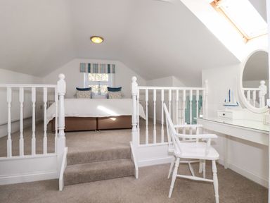 A bedroom with a bed pillows window and a vanity table with a chair and mirror at Great Meadow Barn in Crantock
