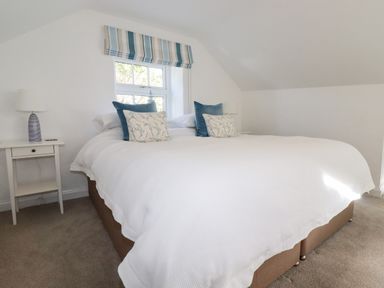 A bedroom with a large bed and pillows with a window and bedside tables at Great Meadow Barn in Crantock